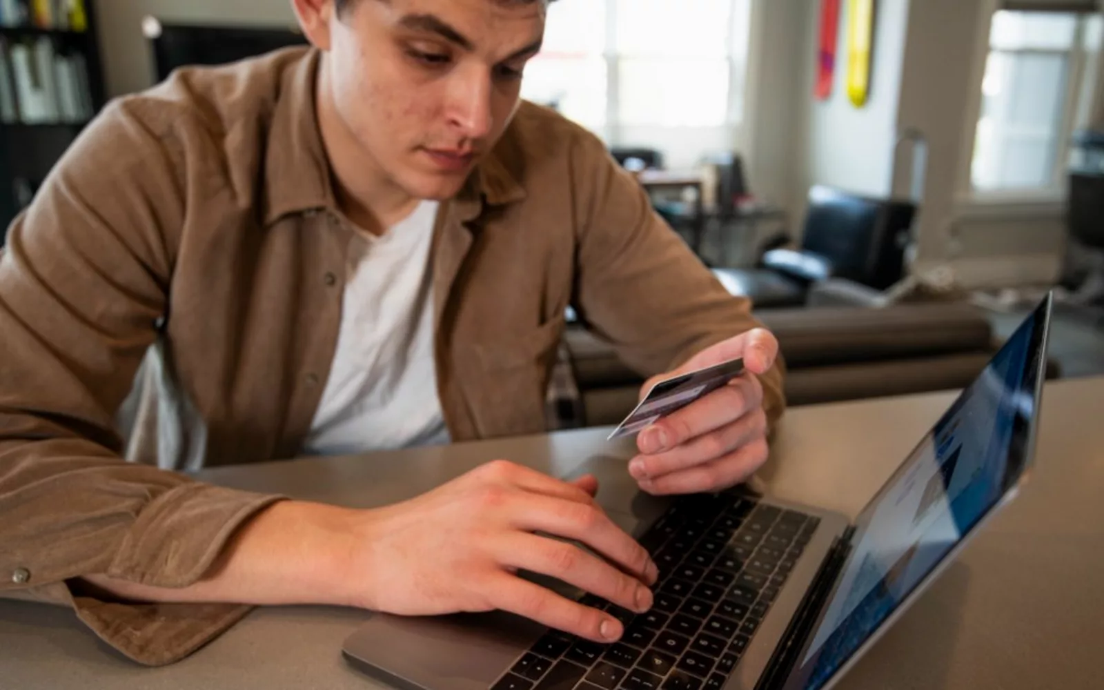 Mężczyzna z kartą płatniczą przy laptopie podczas płatności online